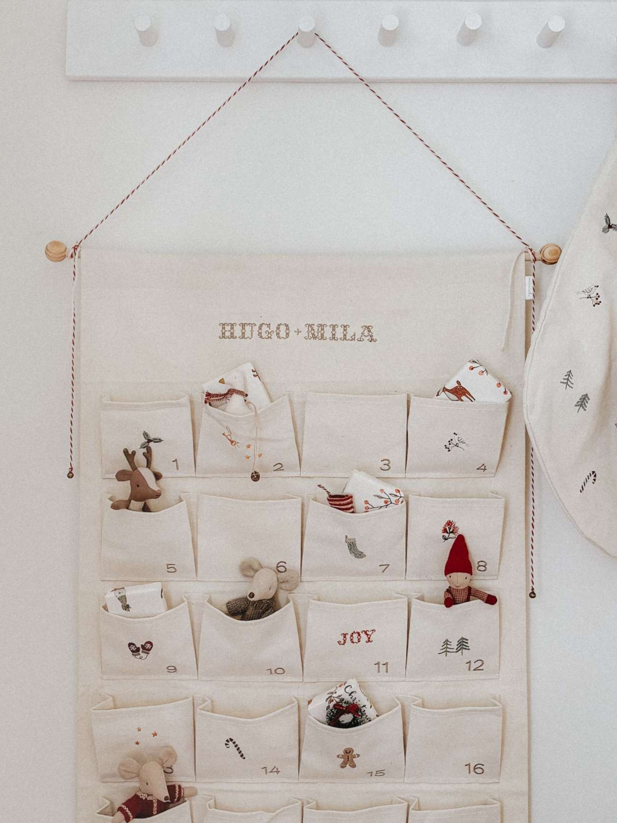 Embroidered Advent Calendar with personalized names, ivory cotton canvas, decorative pockets, and hanging string with tiny bells.