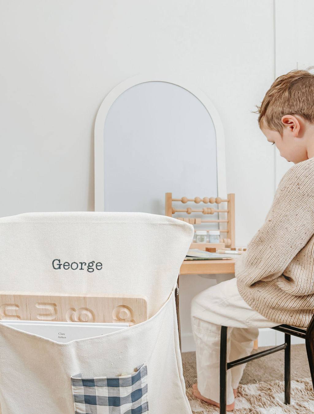 Personalised canvas chair bag with gingham pocket, embroidered with child's name, on small chair.