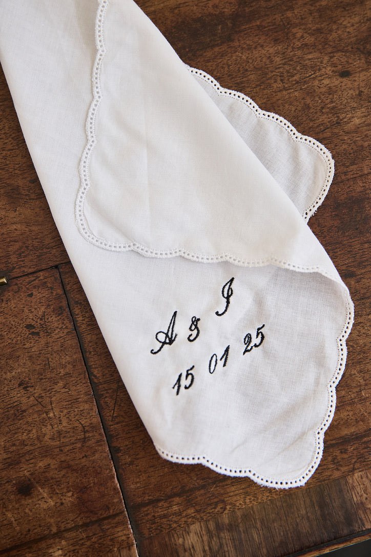 White ladies handkerchief with scalloped edge and custom black embroidery on wooden surface