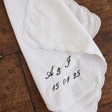 White ladies handkerchief with scalloped edge and custom black embroidery on wooden surface