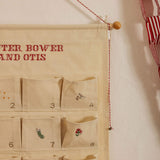 Personalized embroidered advent calendar with Nordic Cross Stitch design on cotton canvas, featuring numbered pockets and hanging wooden dowel.