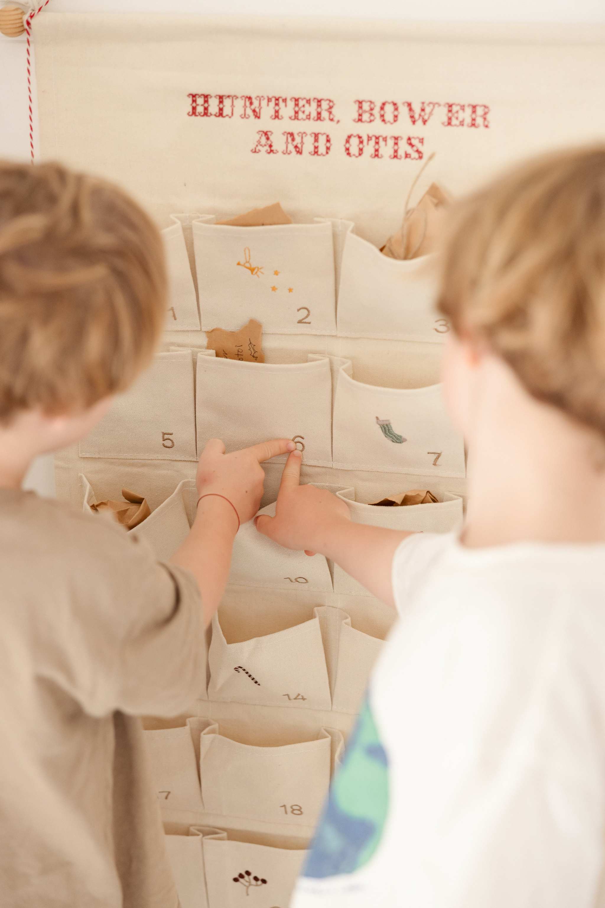 Children using personalized embroidered advent calendar with fabric pockets and red stitched names on cotton canvas