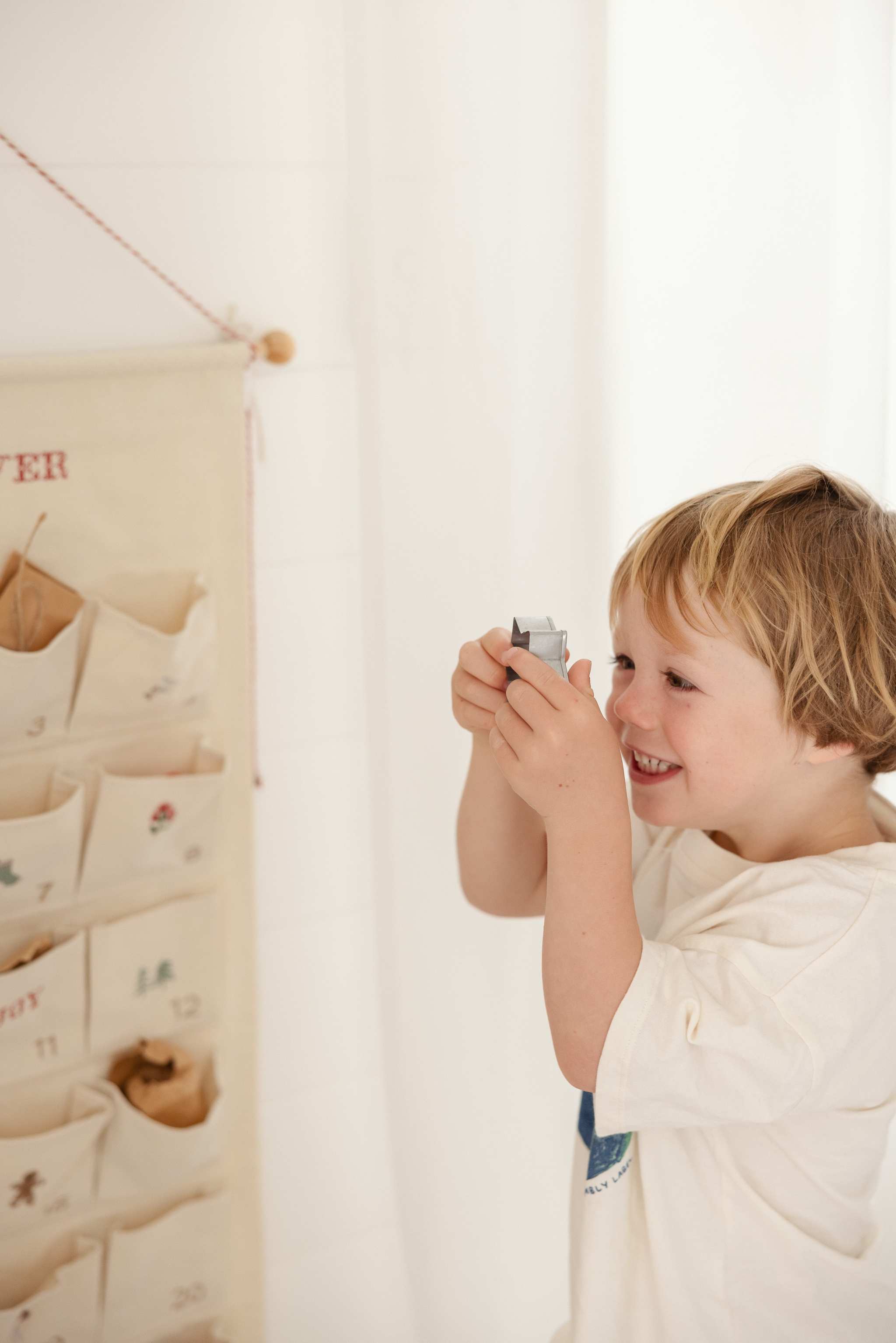 Child playing with personalized embroidered advent calendar hanging on wall with pockets and mini brass bells