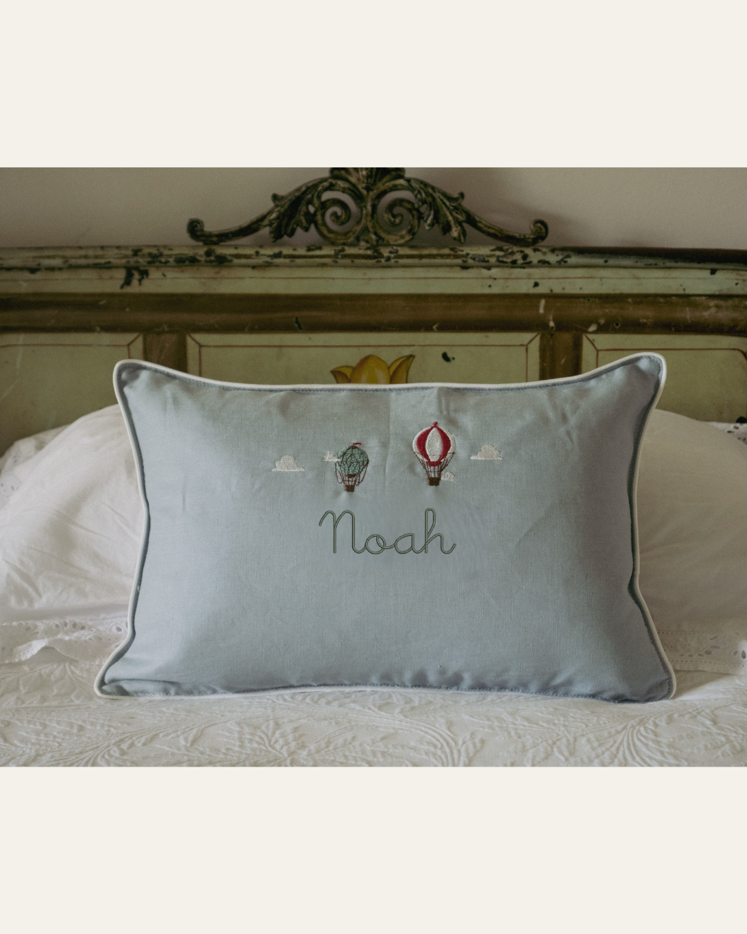 Duck egg blue linen cushion with embroidered vintage hot air balloons and personalized name on bed