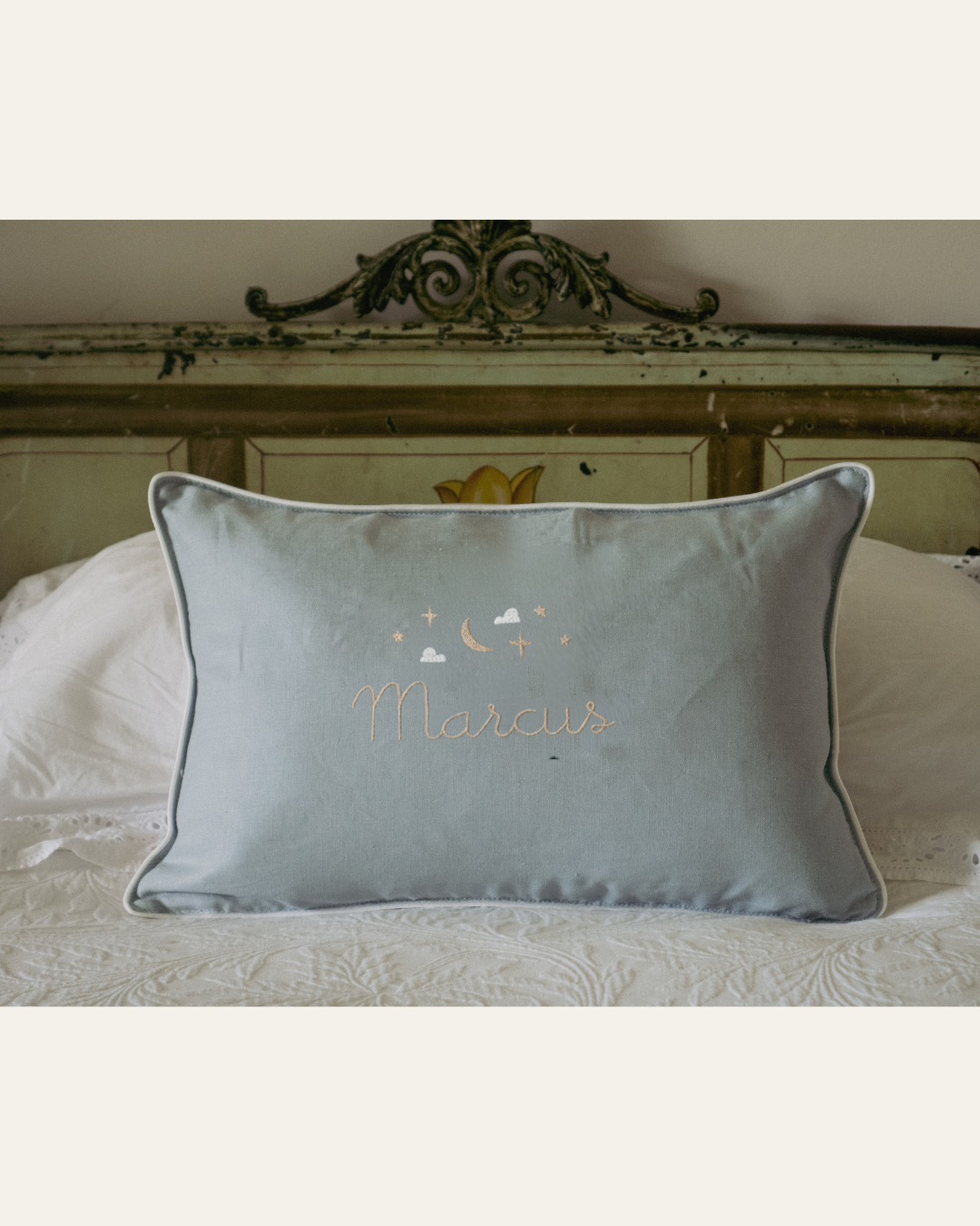 Blue Moon and Stars Cushion with embroidered name, featuring moon and stars needlework, white piping, and removable washable cover on bed