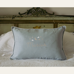 Blue Moon and Stars Cushion with embroidered name, featuring moon and stars needlework, white piping, and removable washable cover on bed