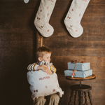 Natural linen Santa sacks with holiday embroidery and personalized names hanging on wall and held by child