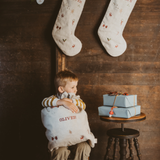 Natural linen Santa sacks with holiday embroidery and personalized names hanging on wall and held by child
