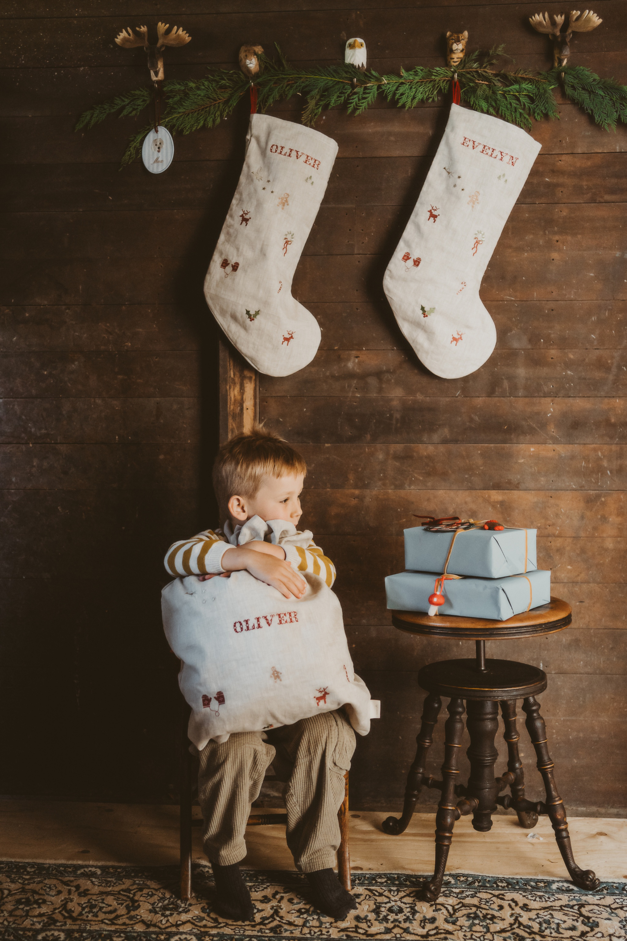 Natural linen Santa sacks with holiday embroidery and personalized names hanging on wall and held by child