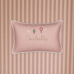 Pink linen cushion with white piping, embroidered hot air balloons and personalized name "Isabella" on striped fabric background