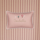 Pink linen cushion with white piping, embroidered hot air balloons and personalized name "Isabella" on striped fabric background