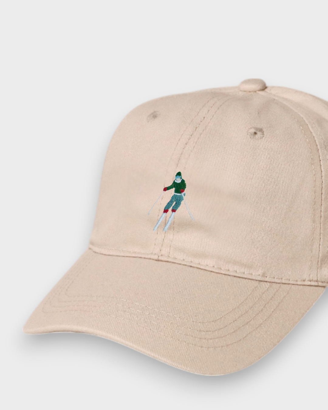 Beige personalised baseball hat with embroidered skier design, made of 100% washed cotton, available in kids and adult sizes.
