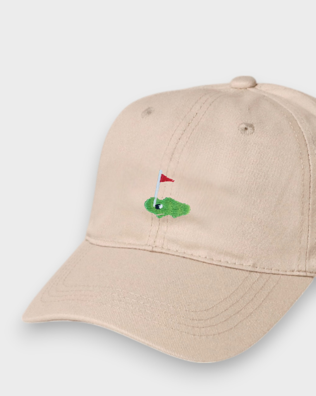 Beige baseball cap with embroidered golf hole and red flag design, personalised text option on back, made from 100% washed cotton.