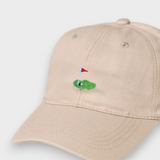 Beige baseball cap with embroidered golf hole and red flag design, personalised text option on back, made from 100% washed cotton.