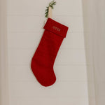 Red plain linen stocking with personalized Nordic cross stitch name hanging on white wooden wall