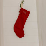 Red plain linen stocking with personalized Nordic cross stitch name hanging on white wooden wall
