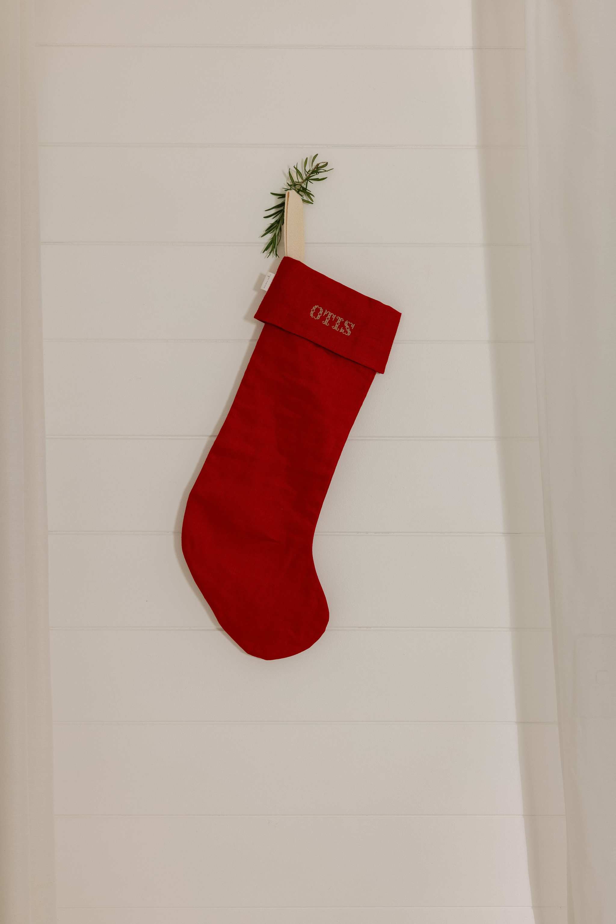 Red plain linen stocking with personalized Nordic cross stitch name hanging on white wooden wall