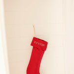 Red plain linen stocking with personalized Nordic cross stitch name hanging on wall