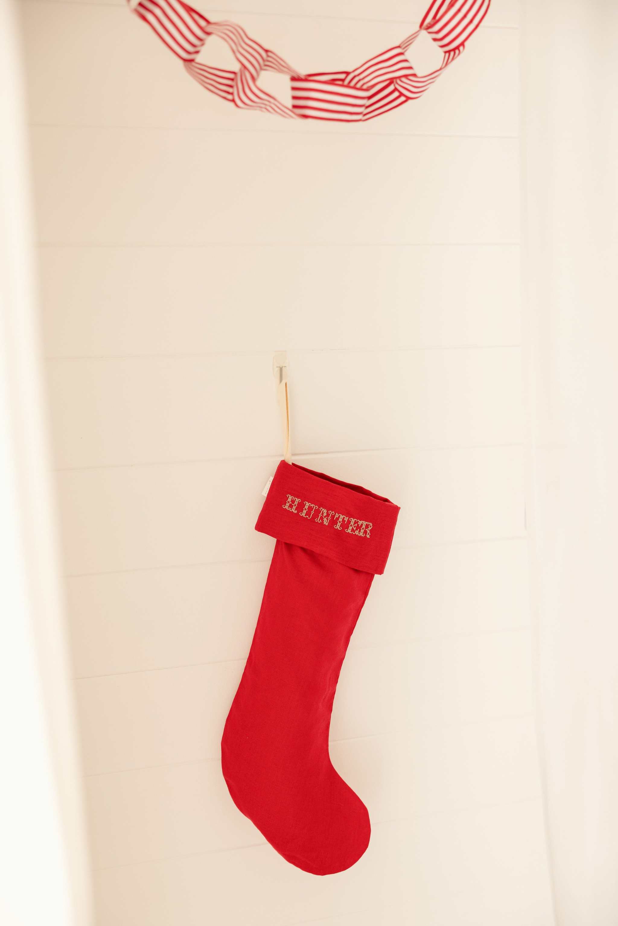 Red plain linen stocking with personalized Nordic cross stitch name hanging on wall