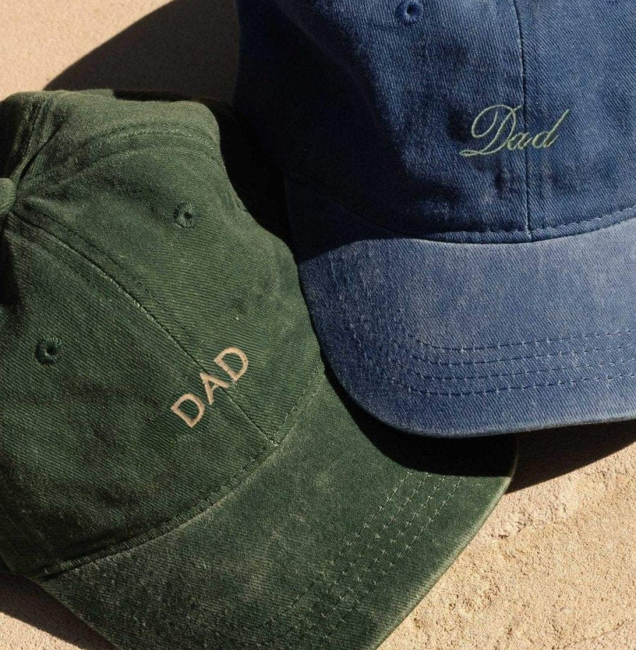 Green Dad cap in block lettering beside a navy Dad cap in script